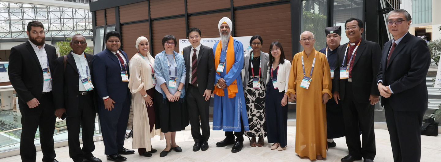 Group of people in diverse religious attire, wearing ID badges, standing indoors.